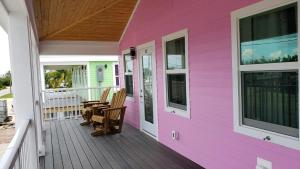 大鬆礁島的住宿－Old Wooden Bridge Resort & Marina，前廊的粉红色房子,配有椅子