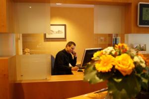 un hombre sentado en un escritorio frente a una computadora en Hotel an der Ilse, en Lemgo