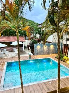 una piscina con 2 palmeras frente a una casa en Pousada Estalagem dos Corais da Prainha, en Arraial do Cabo