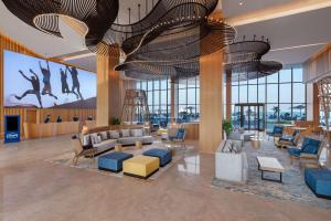 vestíbulo con sofás, sillas y ventanas grandes en Hampton by Hilton Marjan Island, en Ras al Khaimah