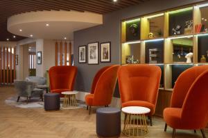 a waiting room with orange chairs and tables at DoubleTree by Hilton London Elstree in Borehamwood