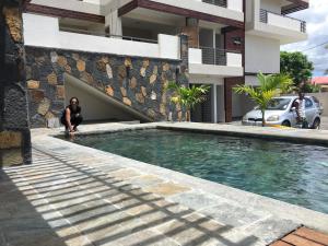 a woman sitting next to a swimming pool next to a building at Beautiful 3 rooms apartment, 2 beds & 1 dressing room in Flic-en-Flac