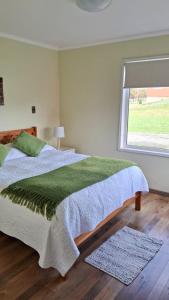 1 dormitorio con 1 cama con manta verde y ventana en Cabañas Puerto Varas, en Puerto Varas