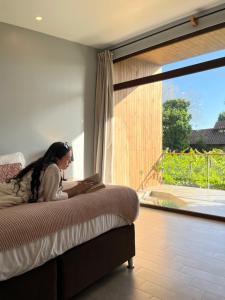 Kobieta siedząca na łóżku patrząca przez okno w obiekcie Parronales de Los Boldos w mieście Santa Cruz