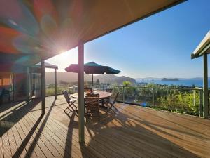 a deck with a table and chairs and an umbrella at Seven Island View in Hahei
