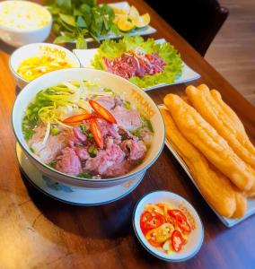 a wooden table topped with a bowl of soup and vegetables at Mon Sapphire Homestay * View Sea and Poem Mountain in Ha Long