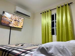 1 dormitorio con cortinas verdes y TV de pantalla plana en Apartamento Amplio en Residencial de 2 Habitaciones, en Mendoza