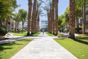 une personne marchant sur un trottoir dans un parc planté de palmiers dans l'établissement FishaRent Luxury Royal Park Suites, à Eilat