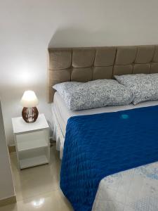 1 dormitorio con 1 cama con manta azul y lámpara en Apartamento Vilage na Praia de Armação Salvador, en Salvador