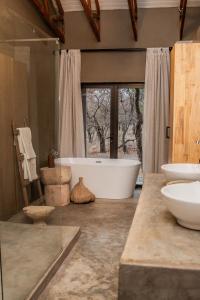 La salle de bains est pourvue d'une baignoire, de 2 lavabos et d'une fenêtre. dans l'établissement Minara Private Boutique Game Lodge, à Dinokeng Game Reserve