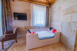 uma banheira num quarto com uma cadeira e uma televisão em Remus Romulus Cappadocia em Üçhisar