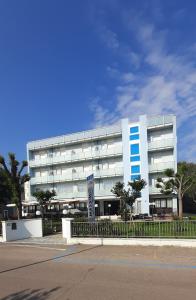 a large white building with blue windows on a street at Hotel Massimo in Cervia