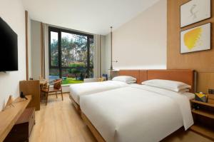 a bedroom with a large white bed and a television at voco Thousand Island Lake, an IHG Hotel in Chun'an