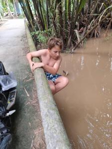 a young boy sitting on a curb in the water at Charming Countryside Homestay in Ben Tre