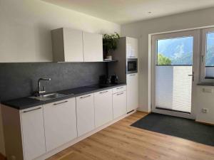 une cuisine avec des placards blancs et une grande fenêtre dans l'établissement Apart Mark, Stanz bei Landeck - Moderne Wohnung in sonniger Lage, à Stanz bei Landeck