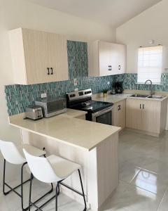 a kitchen with a counter and white chairs in it at Yaad Oasis in Discovery Bay