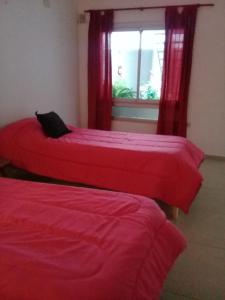 two beds with red sheets in a room with a window at Departamento monoambiente centro pb nuevo sencillo Av Belgrano D3 in Marcos Juárez