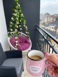 a person holding a cup of coffee on a balcony with a christmas tree at Apartman sa ljuljaskom in Zlatibor