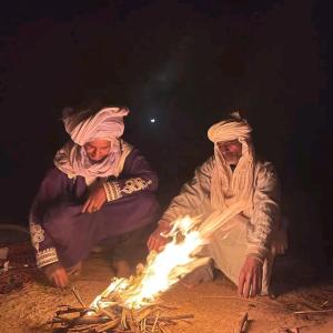 a group of three people sitting around a fire at Desert Waves Excursion in Mhamid