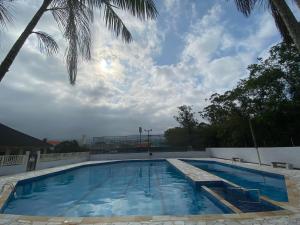 a swimming pool with a palm tree and a cloudy sky at APARTAMENTO EM BERTIOGA in Bertioga