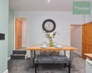 a dining room with a table and a clock on the wall at Stunning Four Bedroom House By PureStay Short Lets & Serviced Accommodation Bradford With Parking in Bradford