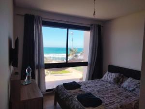 a bedroom with a large window with a view of the ocean at Appartement Plage des Nations Prestigia Front Mer avec grand Jardin in Sidi Bouqnadel