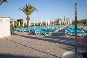 a row of blue chairs and palm trees on a beach at Happy Tavira Apartments - Apartamento Inspire Cabanas no Resort Golden Club in Cabanas de Tavira
