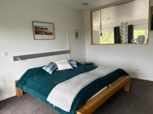 a bedroom with a bed with a green blanket and a mirror at Tutukaka Sunrise in Tutukaka