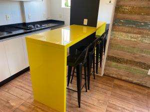 a yellow island in a kitchen with black chairs at Studio Minimalista Região Central Residencial Padre Kolb 201C in Joinville +18 photos