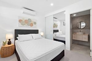 a white bedroom with a bed and a bathroom at Ohana Apartments 103 in Batemans Bay