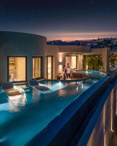 dos personas de pie en una piscina por la noche en Senses Luxury Houses en Fira