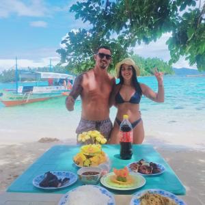 mężczyzna i kobieta stojący obok stołu z jedzeniem na plaży w obiekcie Port Barton Island Camping w mieście San Vicente