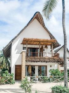 a white house with a balcony and a palm tree at Villa Upendo with pool, Zanzibar in Pingwe