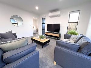 uma sala de estar com dois sofás azuis e uma televisão em Villa in Central Hamilton - By KOSH BNB em Hamilton