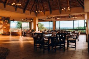 uma sala de jantar com mesas e cadeiras e janelas grandes em Elephant Hills Resort em Victoria Falls