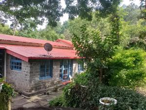 ein Steinhaus mit einem roten Dach und einem Sat-TV in der Unterkunft The Vergomont - A heritage homestay near Nainital in Nainital