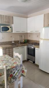 cocina con armarios blancos, mesa y nevera en Casa de 2 quartos no Centro de Bombinhas, en Bombinhas