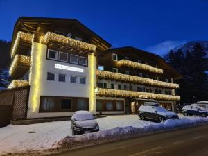 un grande edificio con macchine parcheggiate di fronte di Hotel Rododendro Val di Fassa a Campitello di Fassa