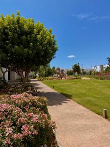 Una pasarela en un parque con un árbol y flores en Luxurious Golf & Sea View Beach Apartment with Pool Access - Cocon de Taghazout Bay, en Taghazout