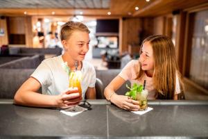 Zwei Mädchen sitzen mit Getränken an der Theke in der Unterkunft Das Bayrischzell Familotel Oberbayern in Bayrischzell