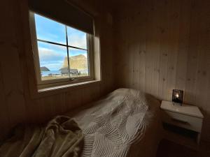 um pequeno quarto com uma cama e uma janela em Tors Cabin at Haukland Beach em Offersøya