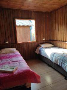 two beds in a room with wooden walls and a window at POUSADA ROTA DOS BALÕES in Praia Grande