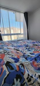 a bed with a colorful comforter on it with a window at Departamento Lynch Iquique in Iquique