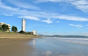 a view of a beach with a building in the background at Lovely 2-Bedrooms Apartment Step to The Beach in Swansea