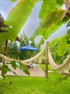a hammock in a garden with a table and an umbrella at Casa Hibiscus Beach Club Ipioca Maceió in Maceió