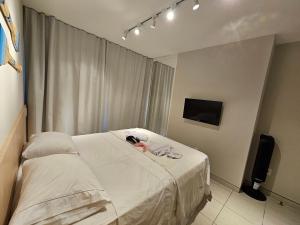 um quarto com uma cama com lençóis brancos e uma televisão em Flat Luxo Térreo com varanda privativa no Nannai e com Varanda Gourmet - LocarHouse em Porto de Galinhas