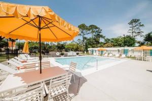 uma piscina com uma mesa e um guarda-sol e cadeiras em Gulf Shores Getaway steps away from the pool! em Gulf Shores
