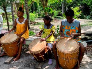 three young children playing drums on a bench at Palmento Grove Garifuna Eco-Cultural & Healing Institute in Hopkins
