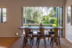 a dining room with a table and chairs and a large window at Paradise on Palm - Stay Waiheke in Palm Beach