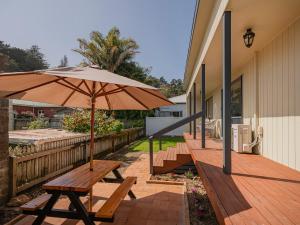 eine Holzbank mit einem Regenschirm auf einer Terrasse in der Unterkunft Gold'n Thames - Thames Holiday Home in Thames